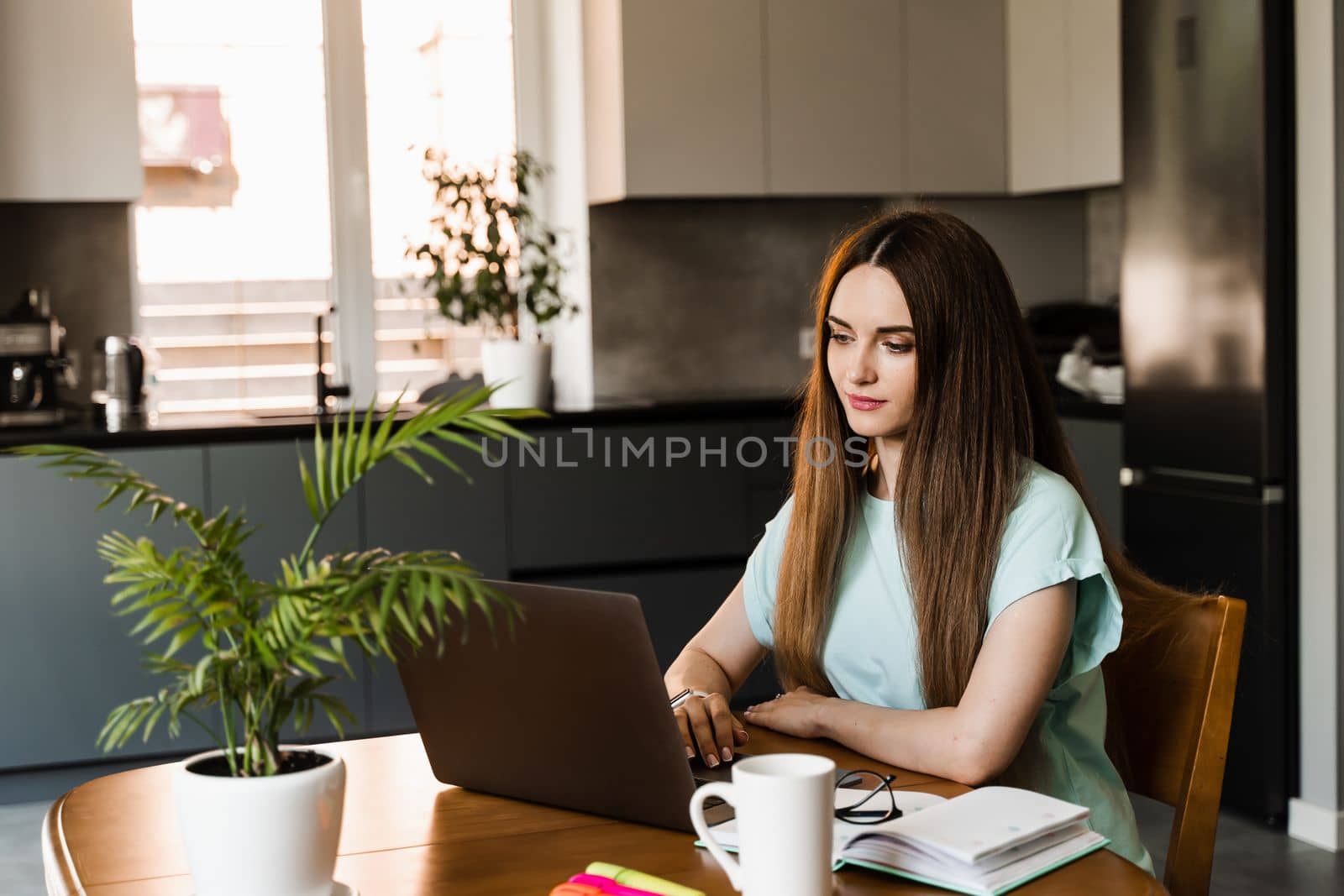 Cheerful young woman programmer works remotely on laptop and try to meet deadline at home. Candid girl with laptop is smiling and rejoices at successful work in IT company. by Rabizo