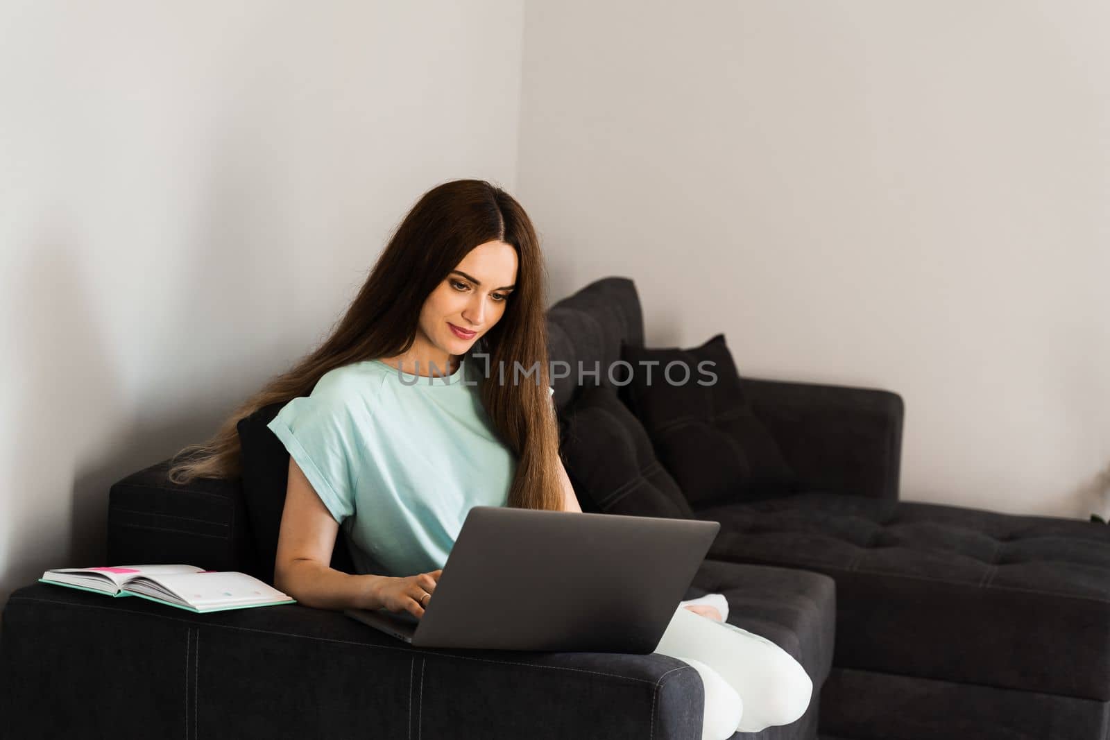 Cheerful young woman programmer works remotely on laptop and try to meet deadline at home. Candid girl with laptop is smiling and rejoices at successful work in IT company. by Rabizo