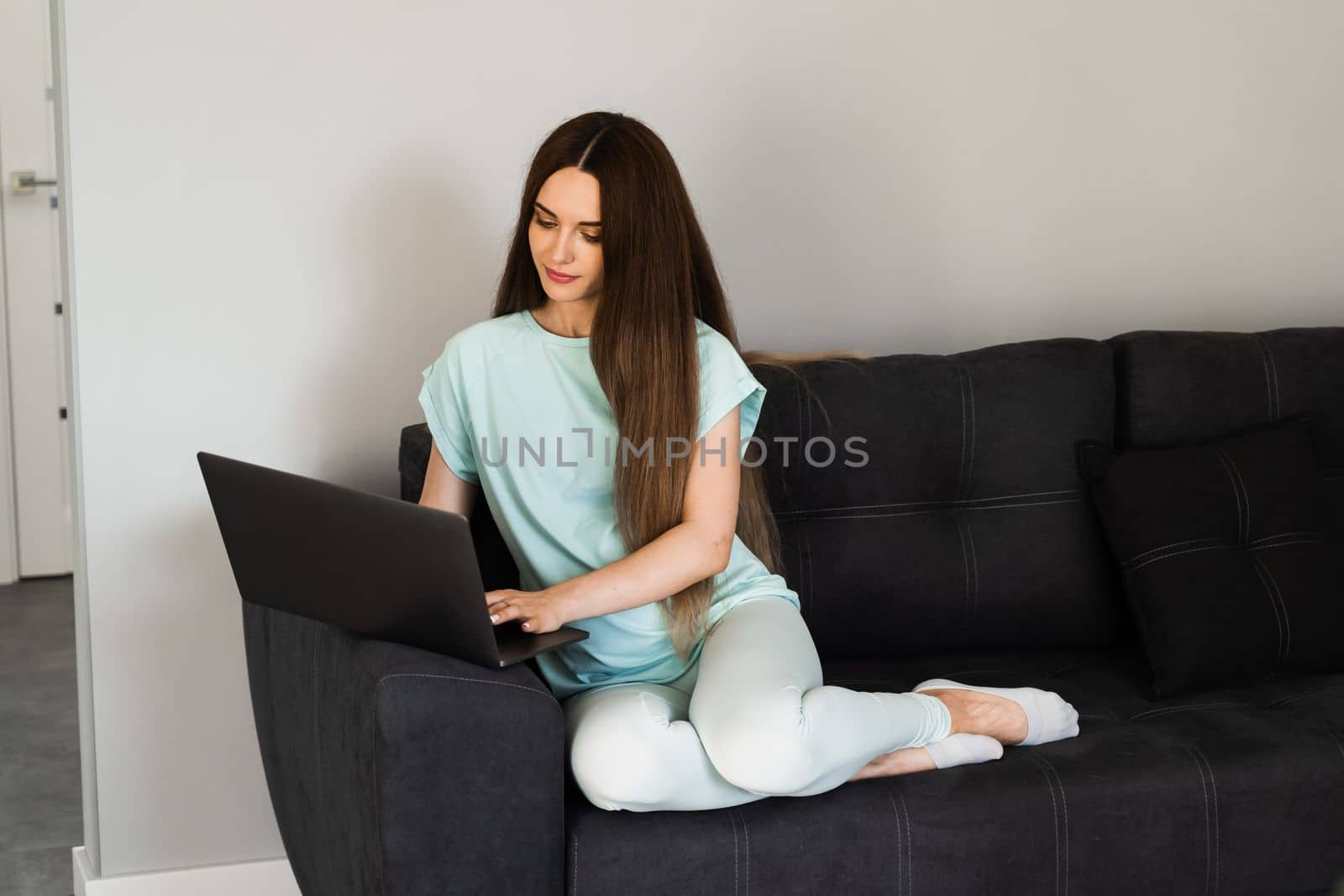 Cheerful young woman programmer works remotely on laptop and try to meet deadline at home. Candid girl with laptop is smiling and rejoices at successful work in IT company. by Rabizo