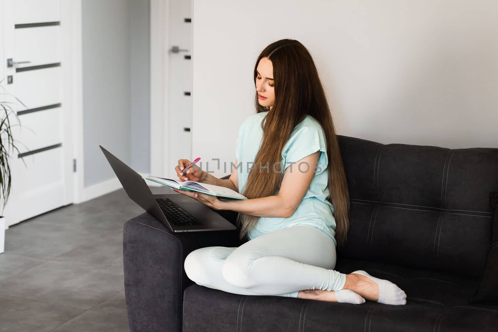 Busy girl with laptop working online at home. Young business woman is sitting on sofa and thinking about creative idea of new project and noticing best ideas