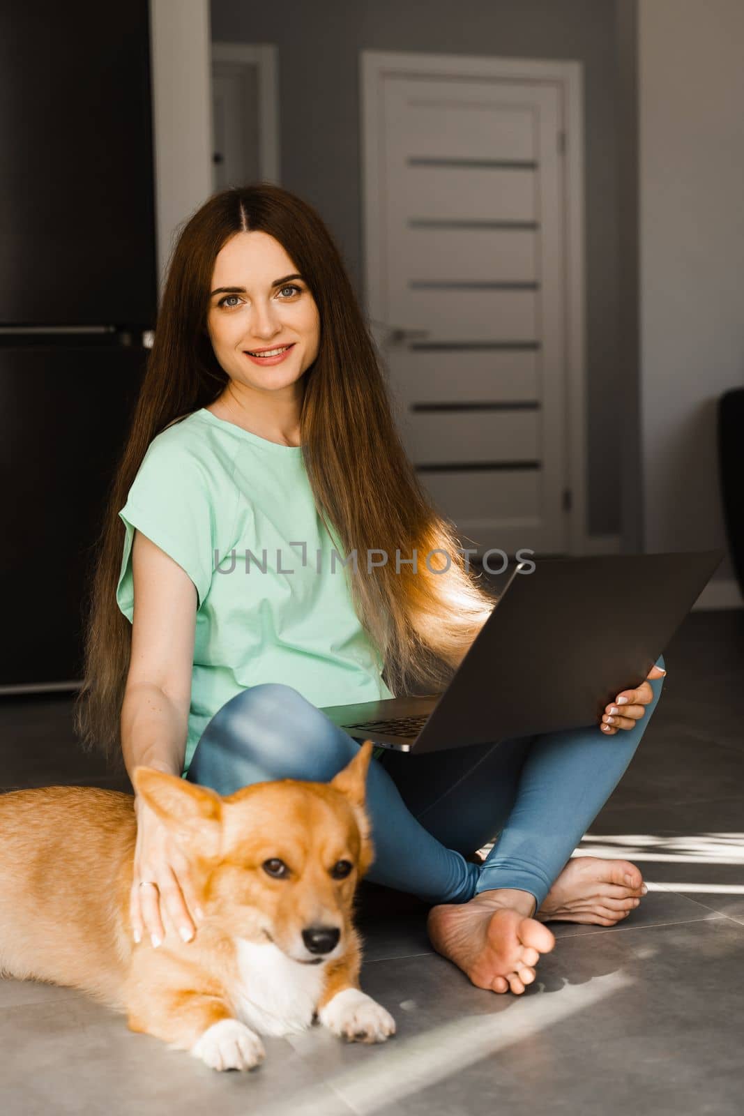 Attractive girl with laptop and Corgi dog sitting on the floor and chatting online with friends. Communication with family and having fun with dog together. Lifestyle with Welsh Corgi Pembroke