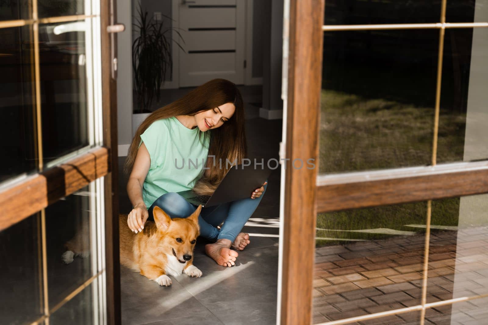 Attractive girl with laptop and Corgi dog sitting on the floor and chatting online with friends. Communication with family and having fun with dog together. Lifestyle with Welsh Corgi Pembroke