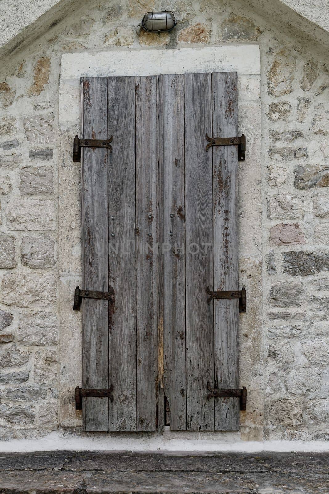 An old weathered, rustic wooden entrance gate made of two wings with solid fittings and an old lamp above the door.