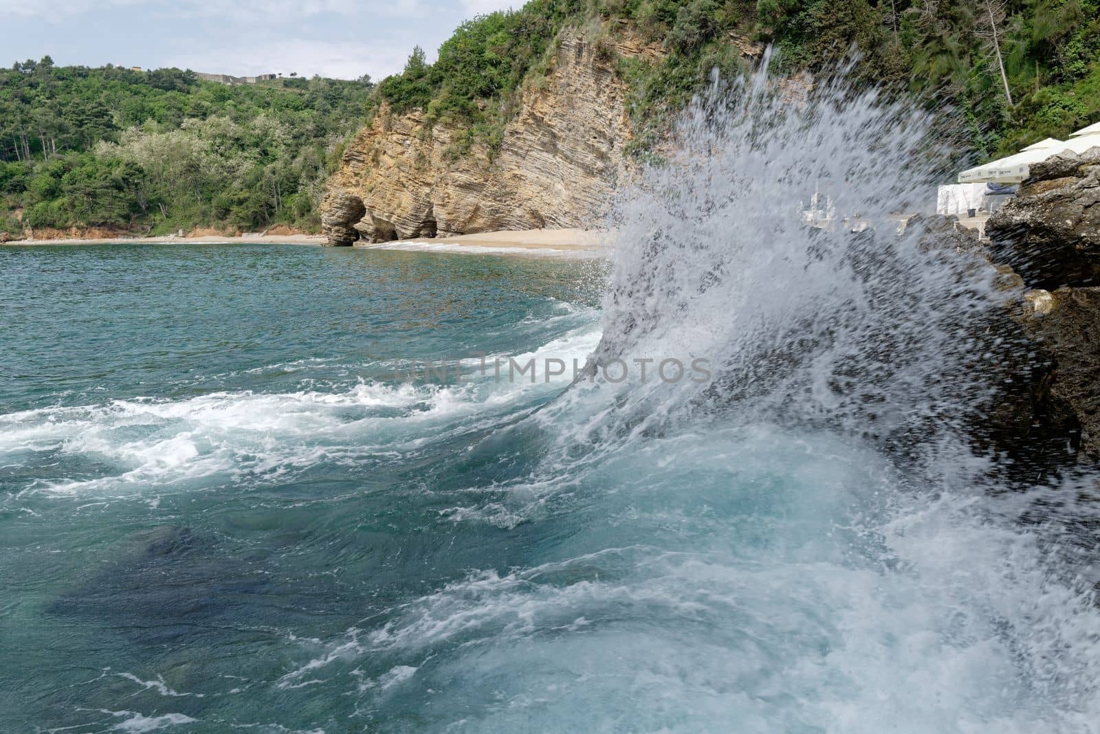 On a rock on the beach, a large wave breaks and creates a beautiful spray.