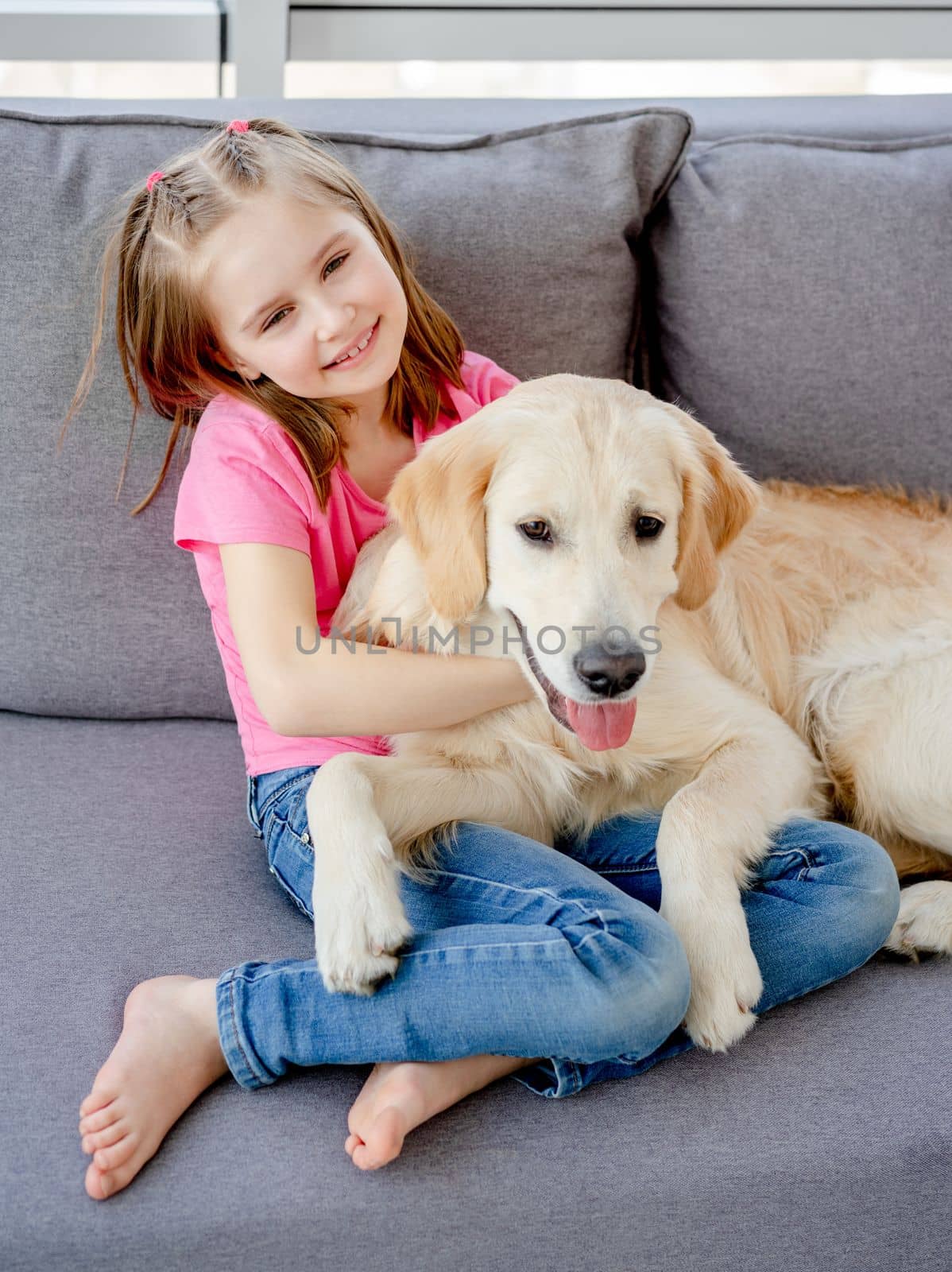 Cute little girl cuddling playful dog at home