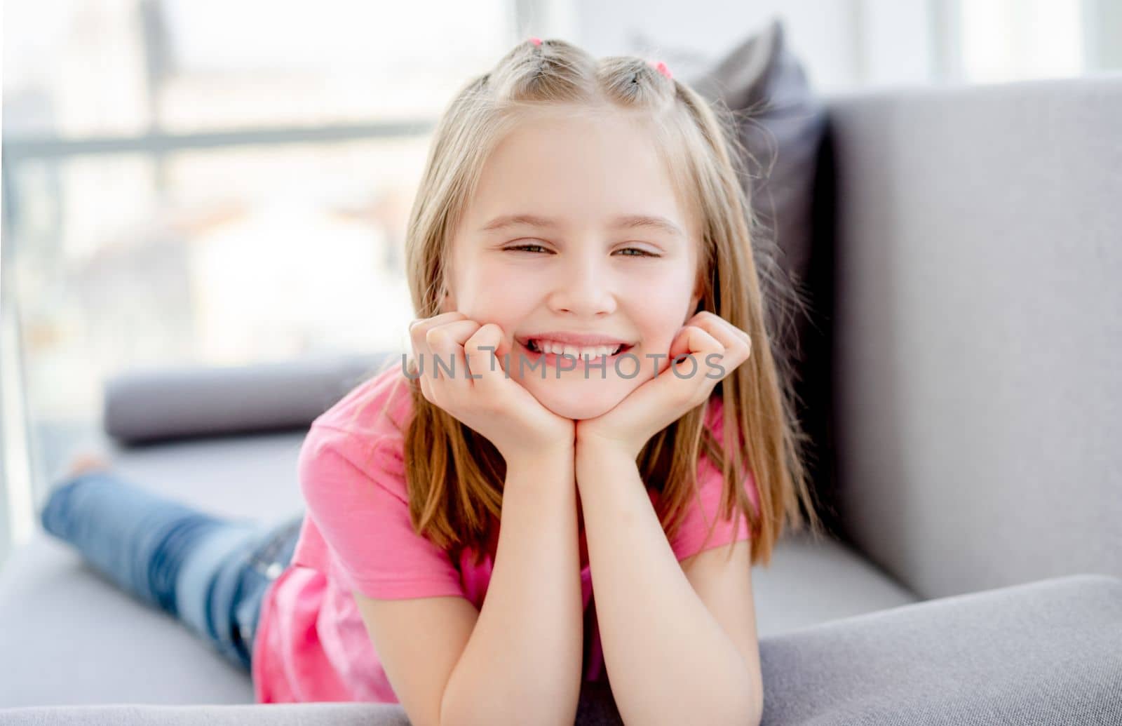 Smiling little girl lying on sofa in bright apartment