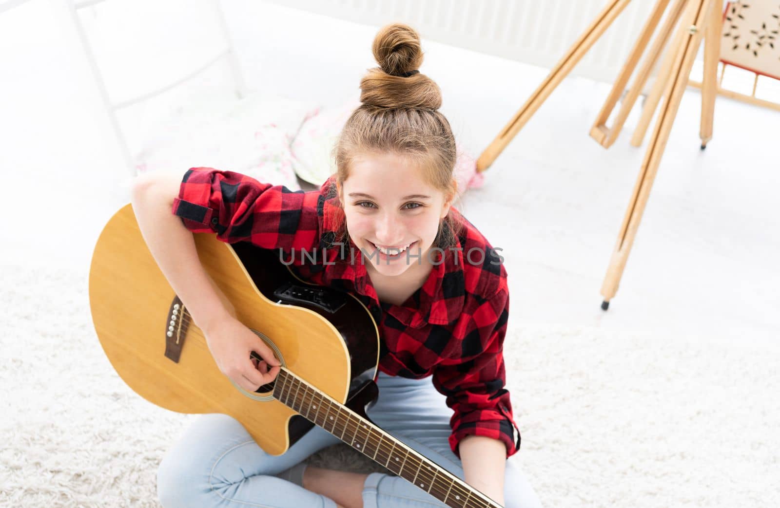 Smiling girl guitarist with musical instrument looking up from floor