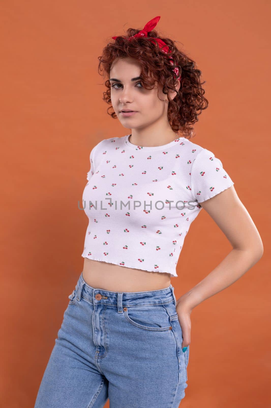 The menacing look of a young girl. Curly chestnut-colored hair. European woman with light Caucasian skin complexion. Isolated from the uniform background.