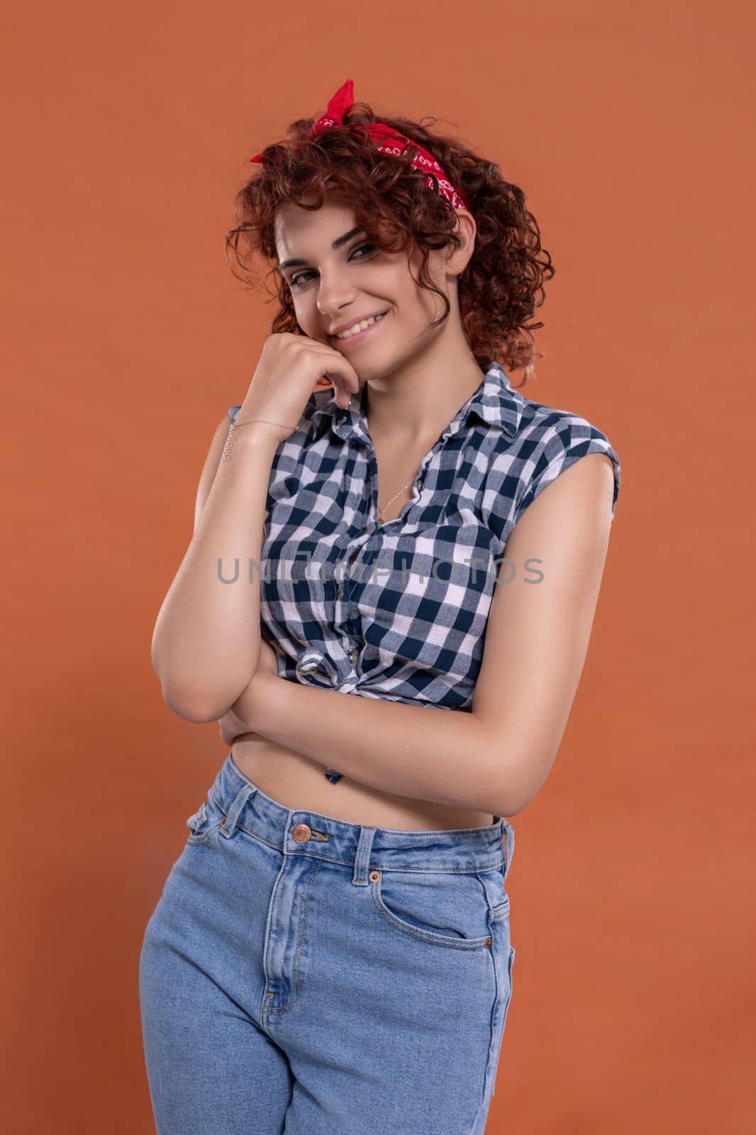 Pin up styling. Girl wearing plaid shirt and tied at the bottom. Short curly hair in chestnut color. Isolated from the uniform background.