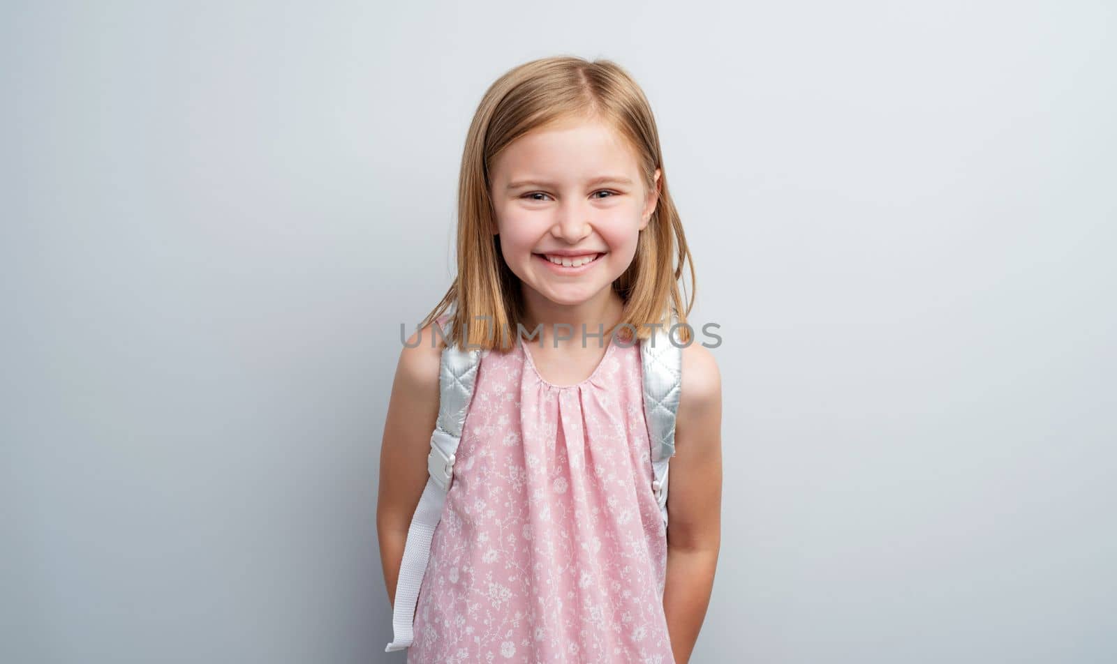 Schoolgirl with backpack posing on gray background