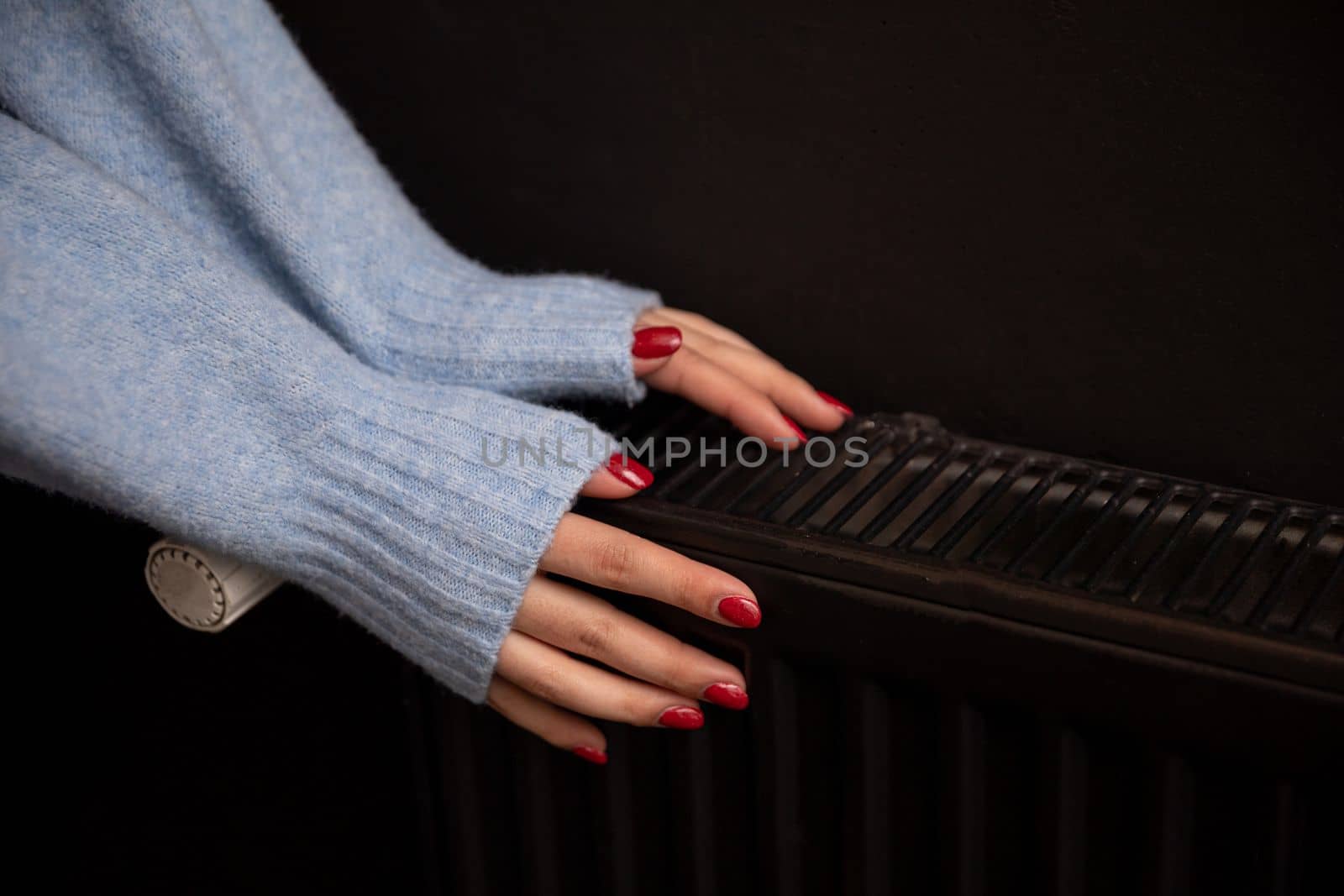 Women's hands touch the radiator to get warm. Central heating essential in winter. Thermal energy in the home.