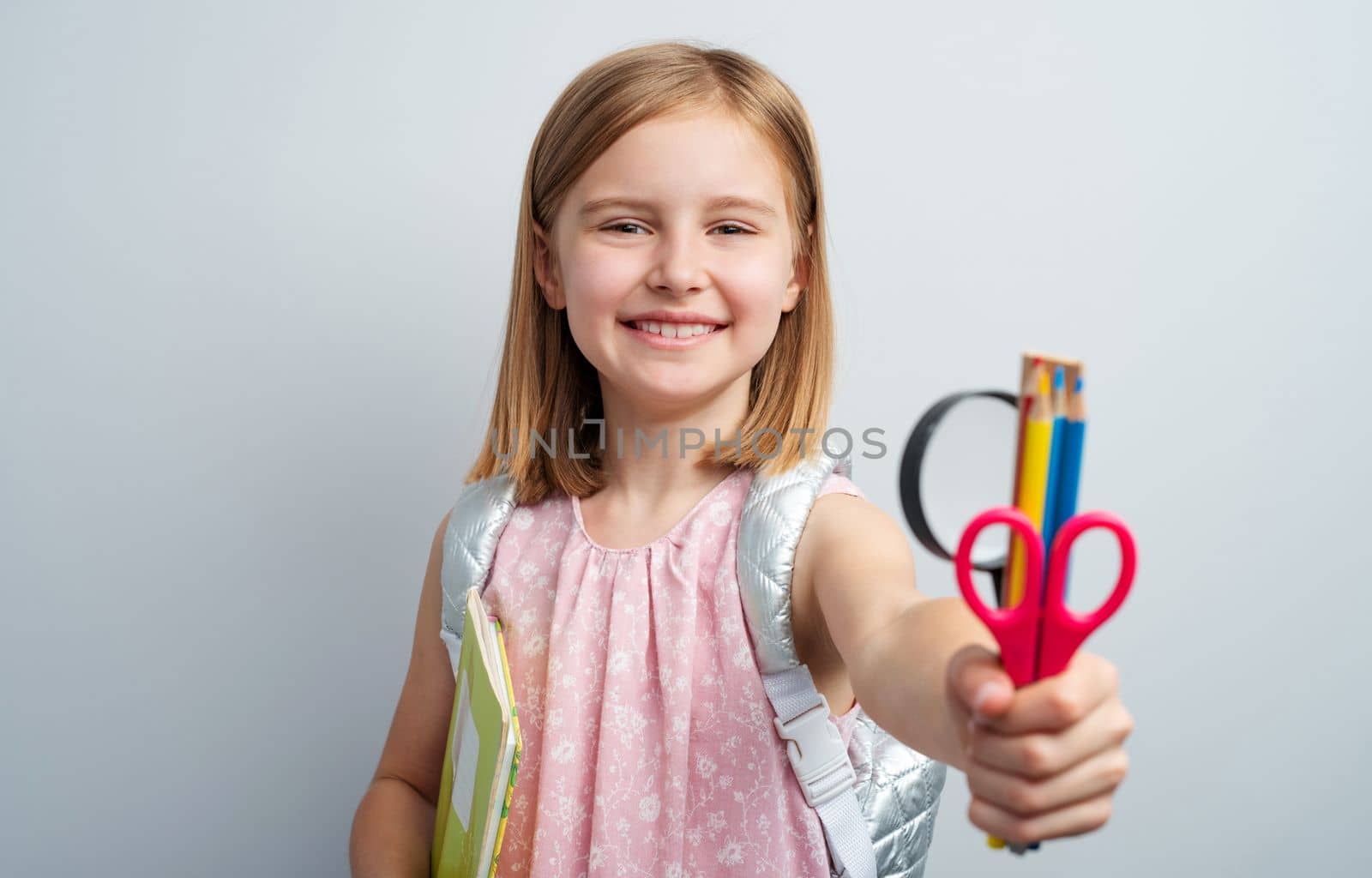 Portrait of schoolgirl with stationery supplies on gray background