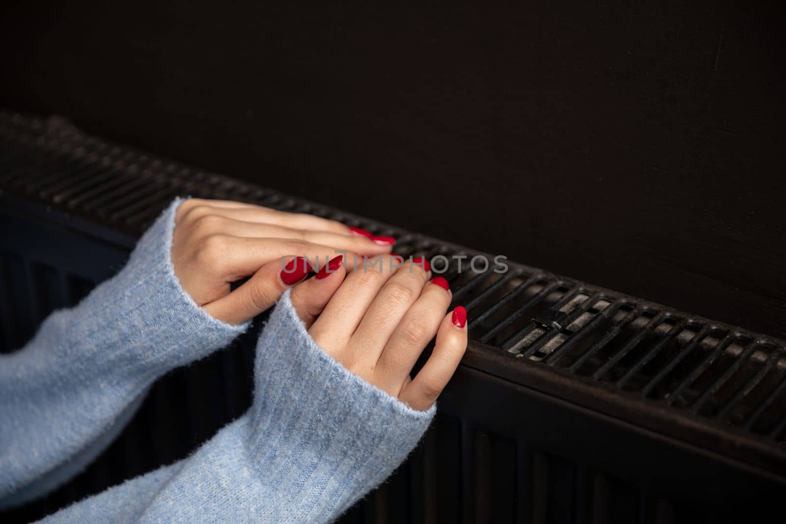 Women's hands touch the radiator to get warm. Central heating essential in winter. Thermal energy in the home.