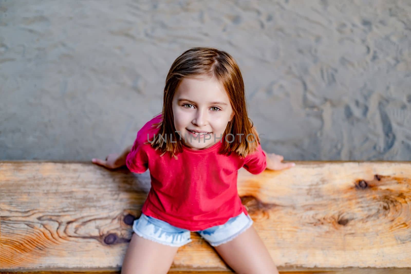 Portrait of smiling little girl sitting on wooden bench, top view
