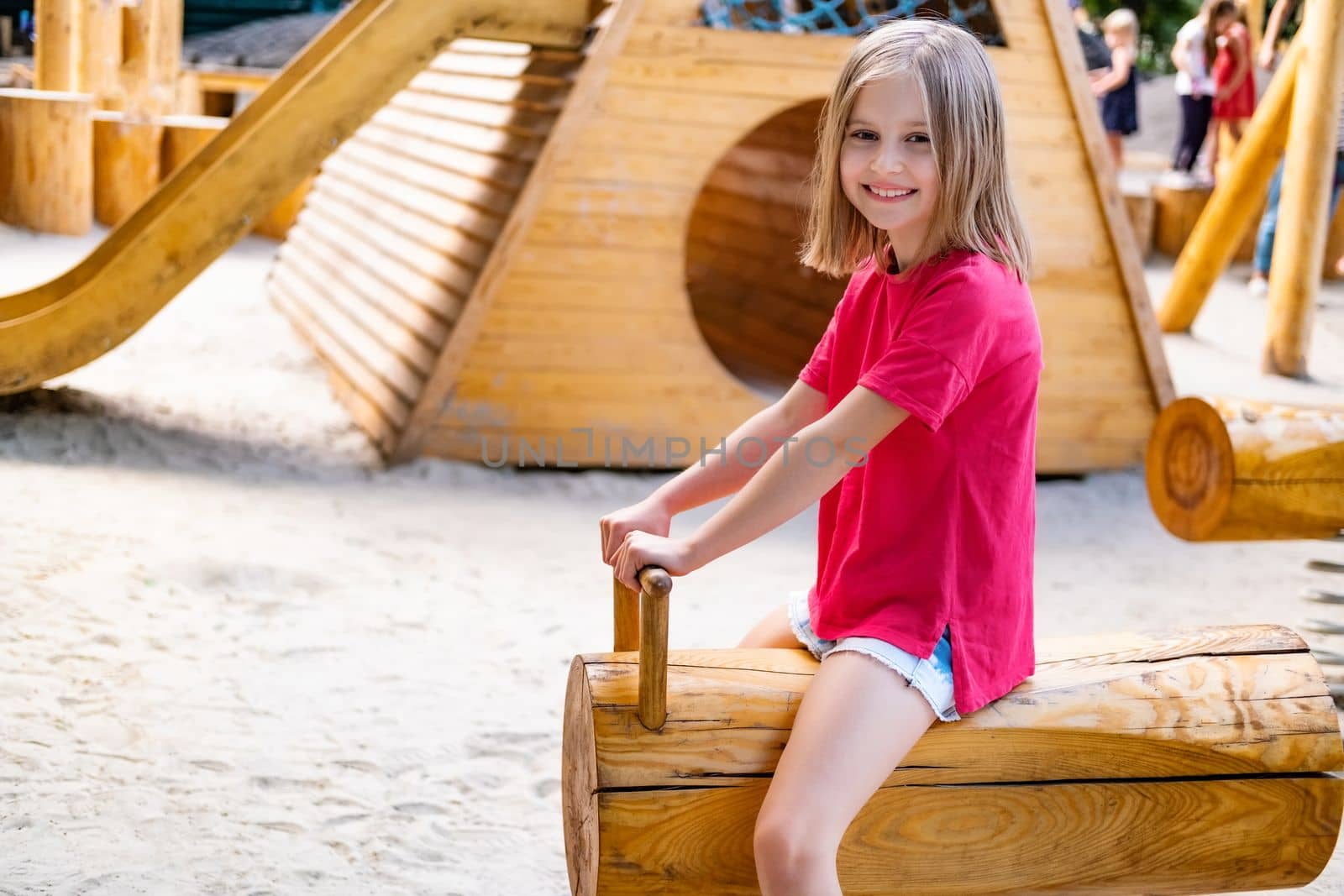 Happy little girl riding wooden swing on kids playground