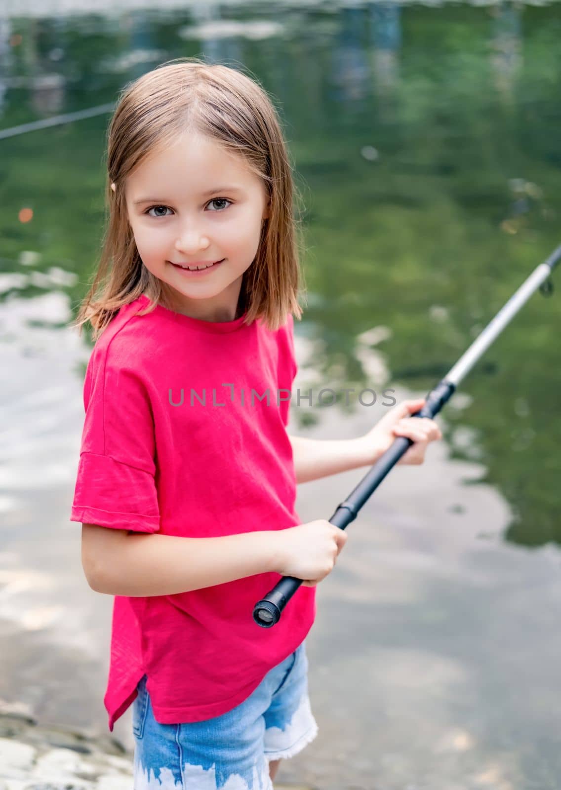 Smiling little girl with rod near river in summer