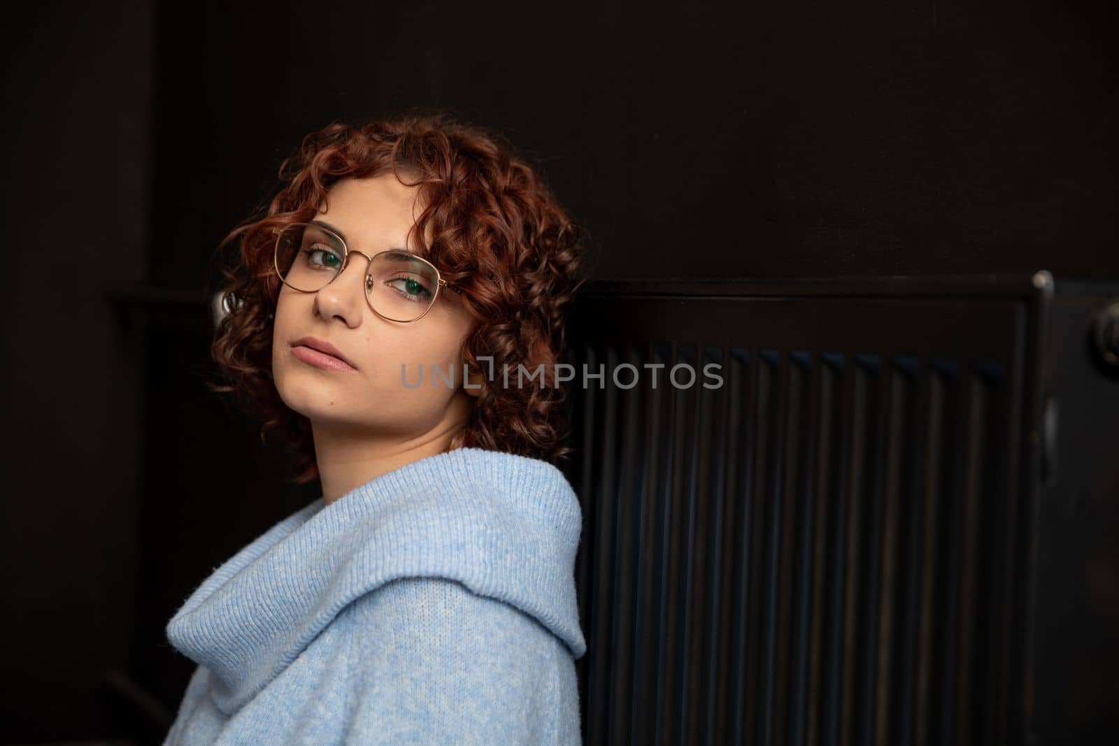 The girl waits by the radiator until the heat appears. The winter period is the time for space heating. Sad and cold if there is a lack of central heating.