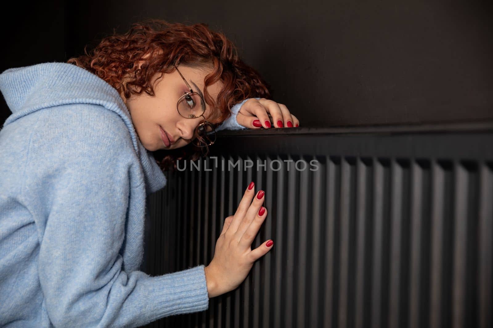 During the winter season and poor heating, the girl hugs the radiator. Central heating necessary in the house during the winter period.