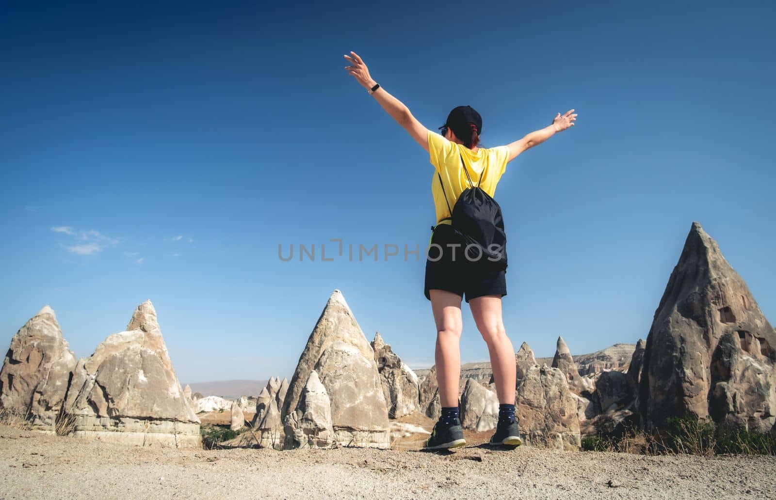 Woman tourist standing back with raised hands on turkish mountains background in Cappadocia