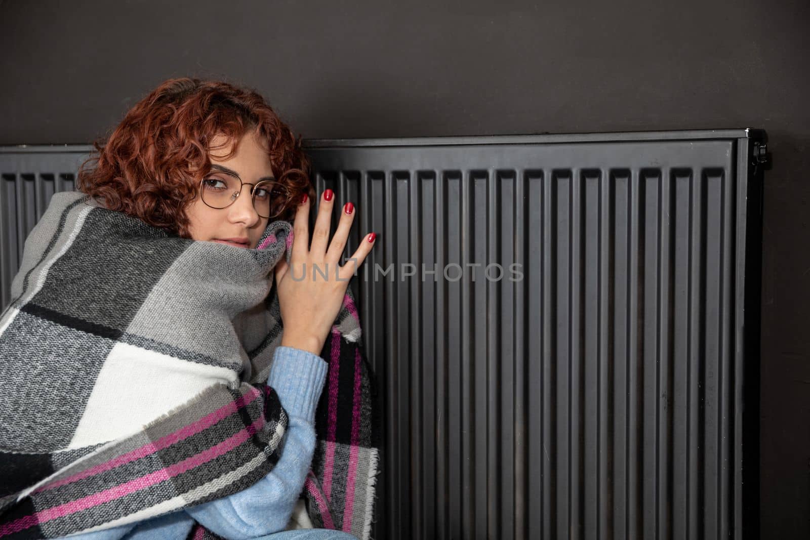 Hot radiator. A girl with curly hair and glasses warms herself at the heater. Central heating during initial startup.