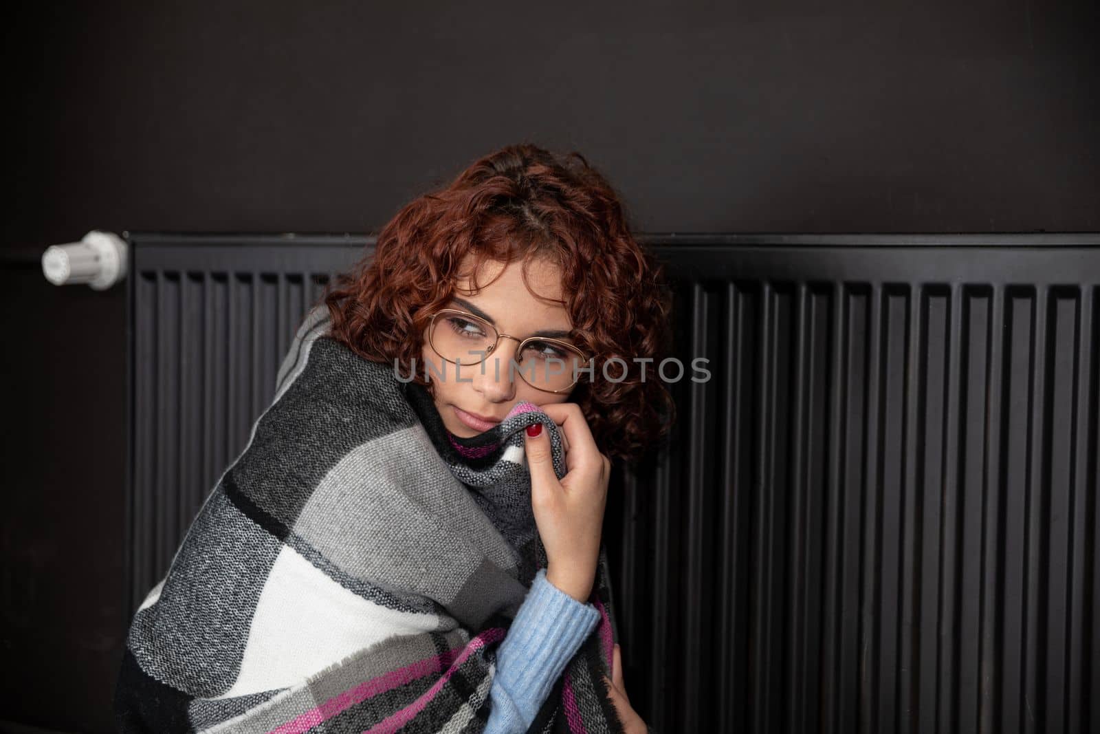Hot radiator. A girl with curly hair and glasses warms herself at the heater. Central heating during initial startup.