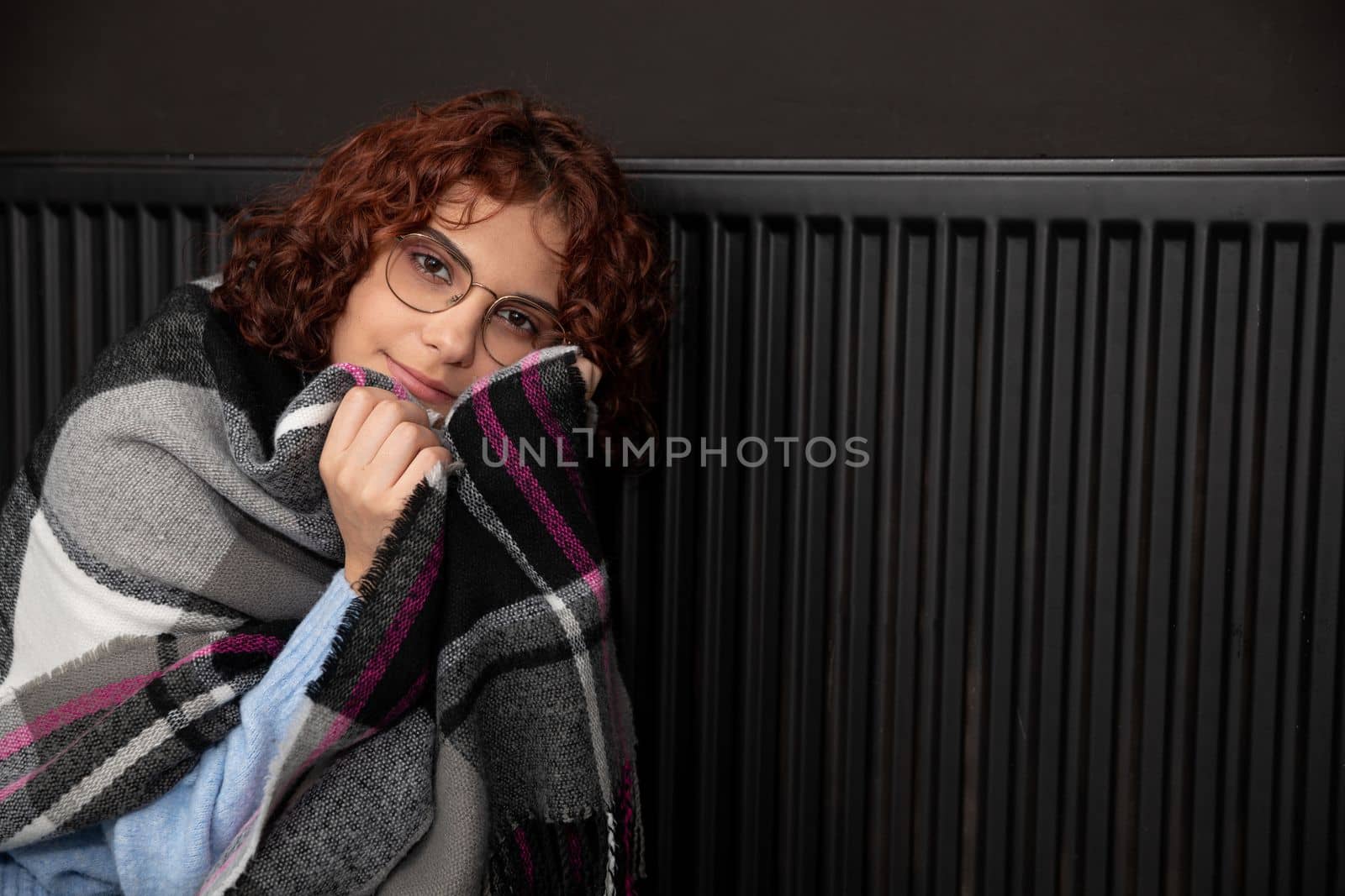 A girl wrapped in a thick scarf. A faulty central heating system. A smiling 20-year-old girl warms herself by the heater.
