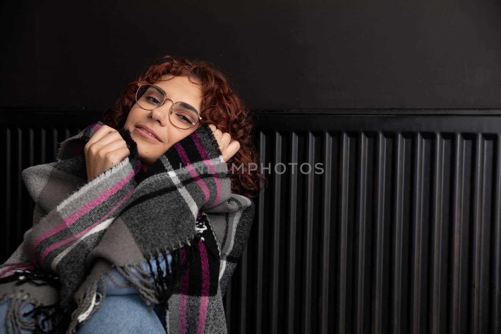 A girl wrapped in a thick scarf. A faulty central heating system. A smiling 20-year-old girl warms herself by the heater.
