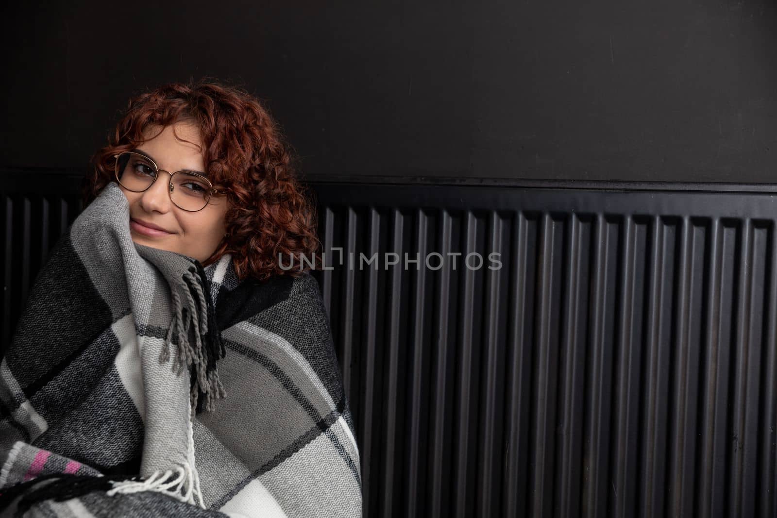A girl wrapped in a thick scarf. A faulty central heating system. A smiling 20-year-old girl warms herself by the heater.