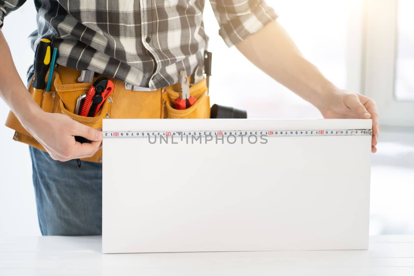 Worker measuring furniture board with measuring tape in workshop