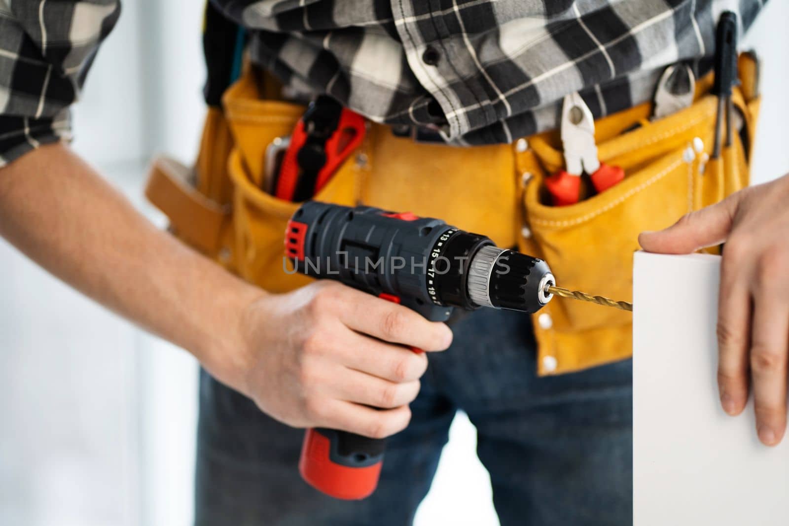 Worker in tool belt drilling furniture board in workshop