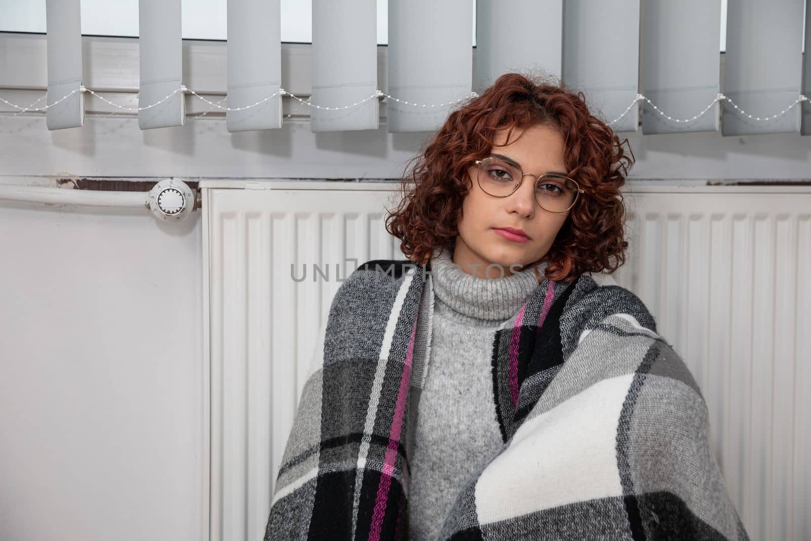 A girl sits wrapped in a scarf hoping the heater will finally start heating. Central heating during the first startup.