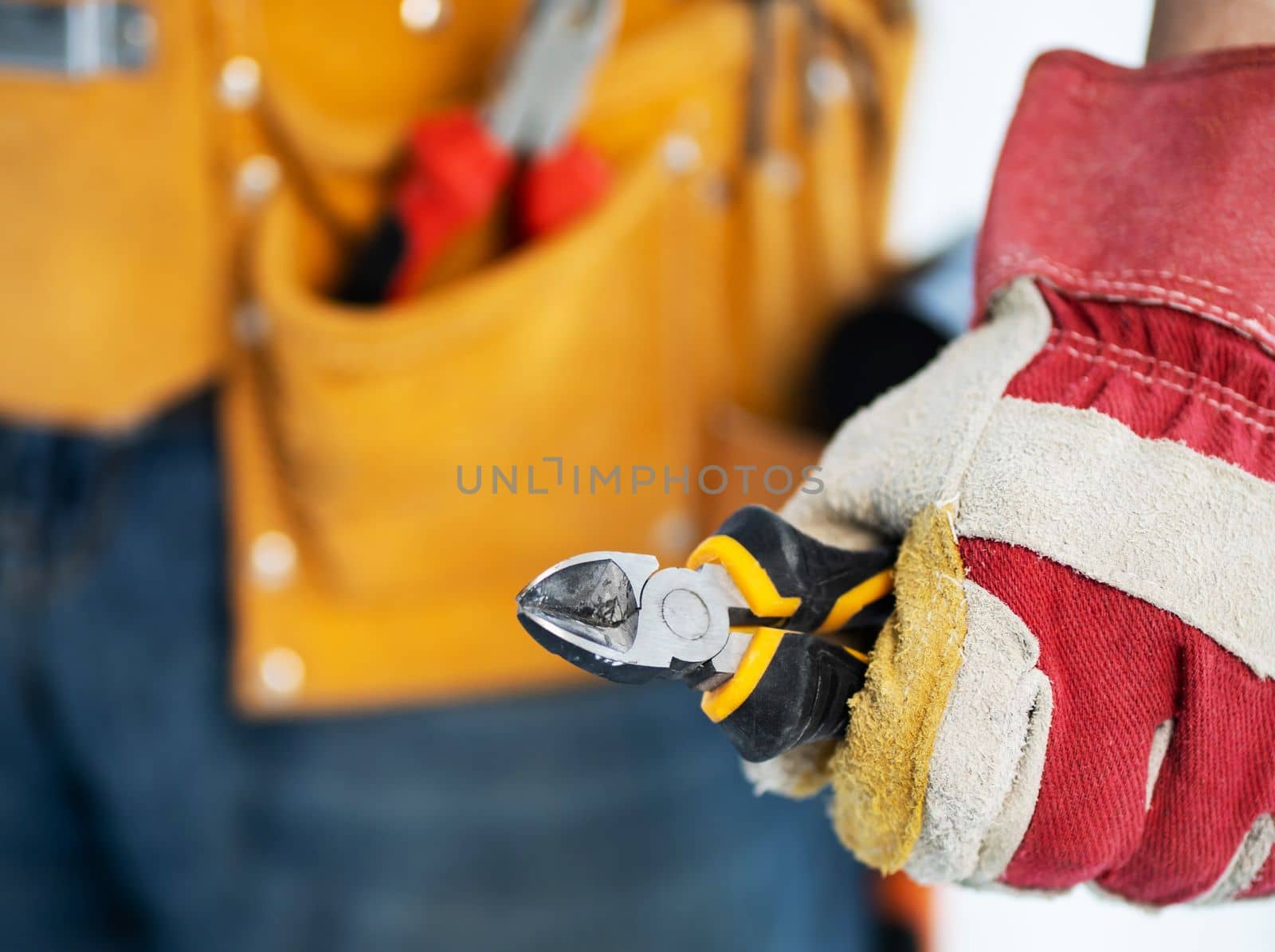 Repairman in assembly belt and protective gloves holding side cutters in hand