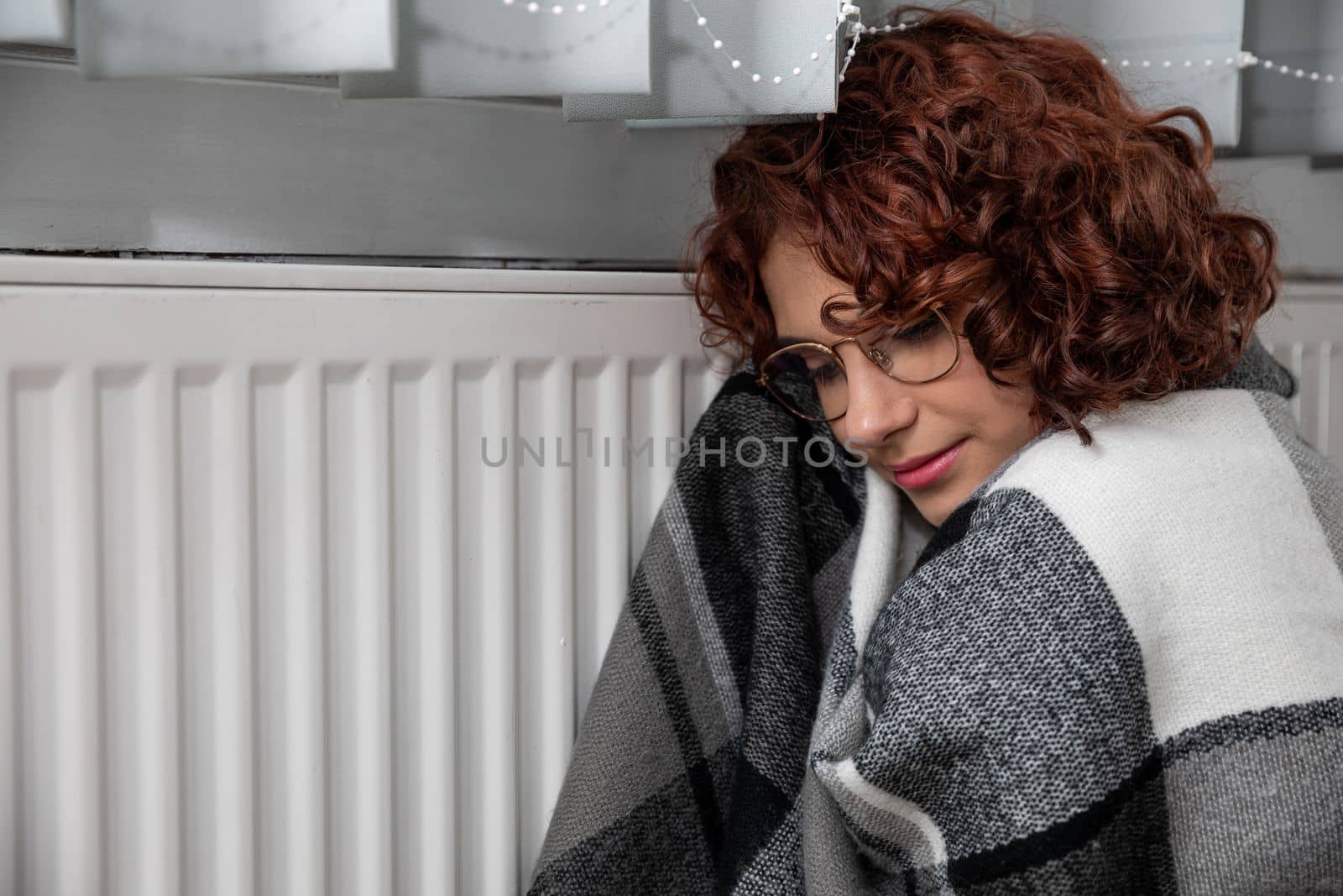 Hot radiator. A girl with curly hair and glasses warms herself at the heater. Central heating during initial startup.