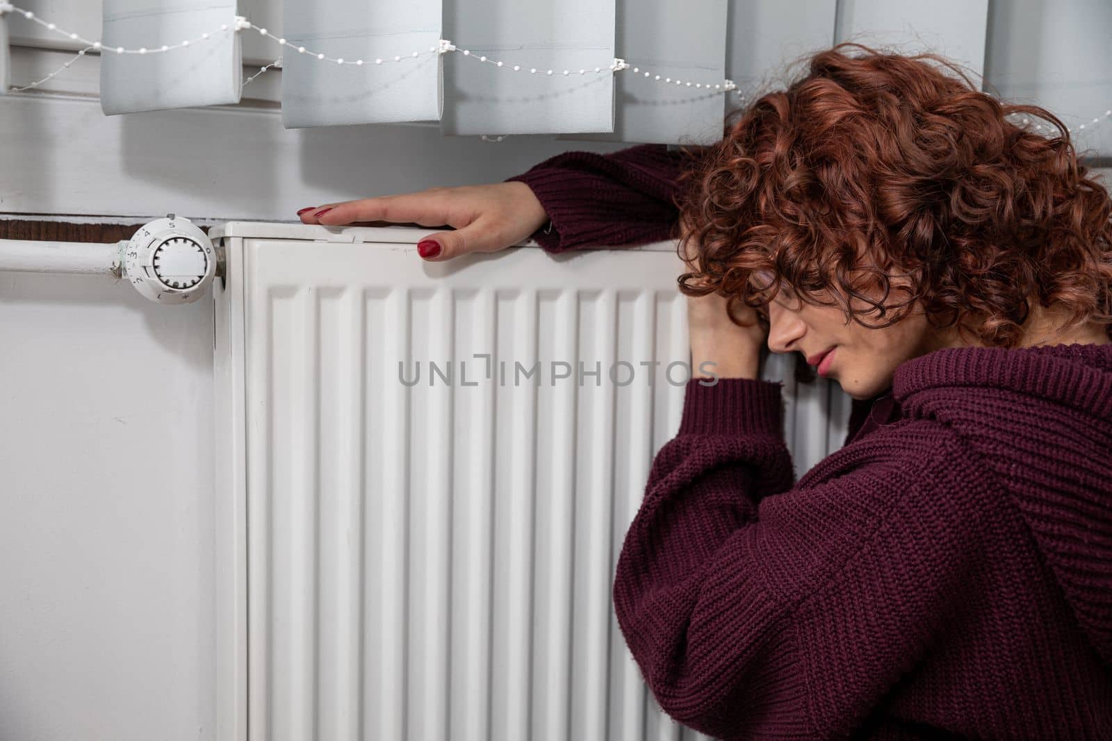 Dressed in a thick sweater, the girl sits on the floor by the radiator hoping that they will finally start the central heating.