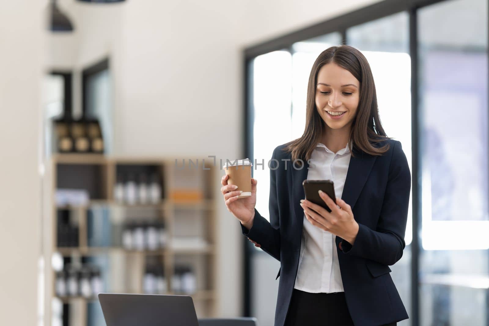 Smiling businesswoman using phone in office. Small business entrepreneur looking at her mobile phone and smiling.