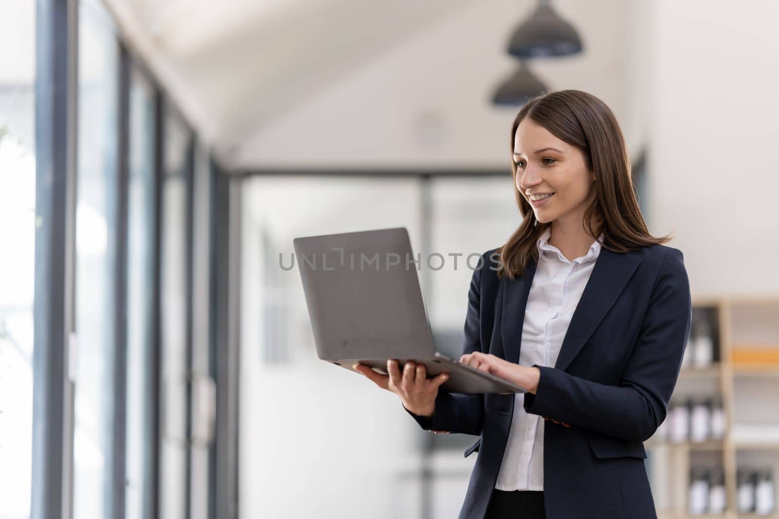 Portrait of a happy businesswoman holding laptop computer on office background.