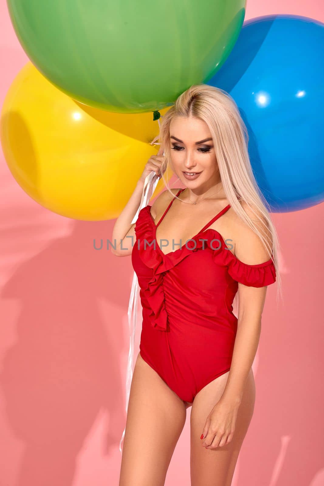 Young sexy slim woman in a red swimsuit with balloons in her hand is posing in a studio. by nazarovsergey