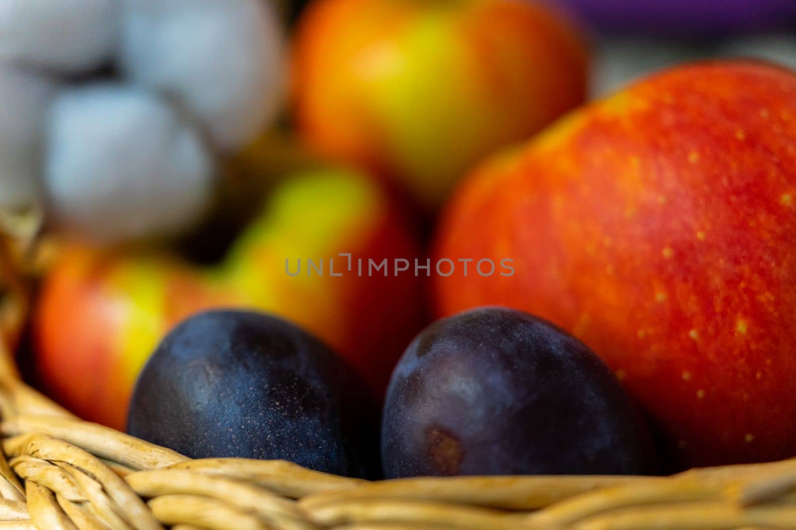 Two ripe plums close-up on a background of red apples. Selective focus by Serhii_Voroshchuk