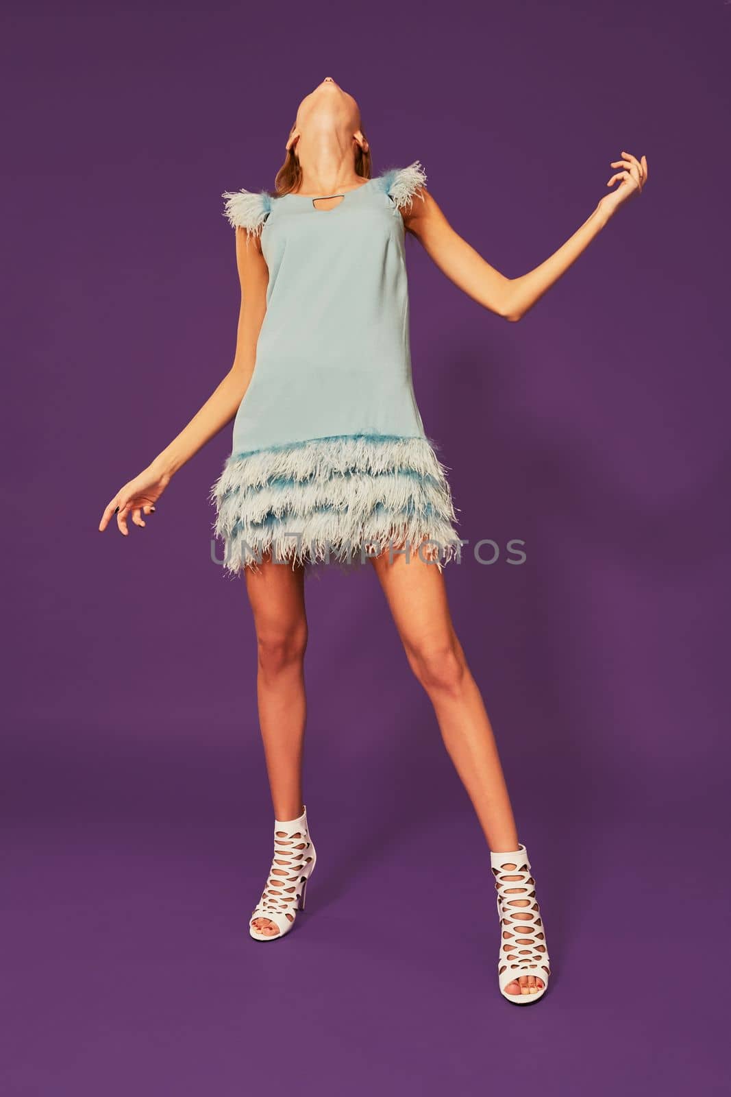 Image of pretty young blonde girl in blue cocktail dress dancing on purple background in studio by nazarovsergey