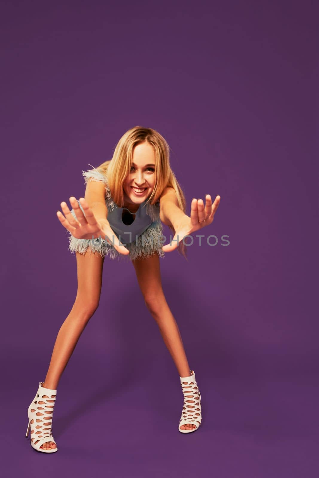 Photo of pretty young blonde girl in blue cocktail dress, trying to keep her balance. Fashion art photo shoot in studio