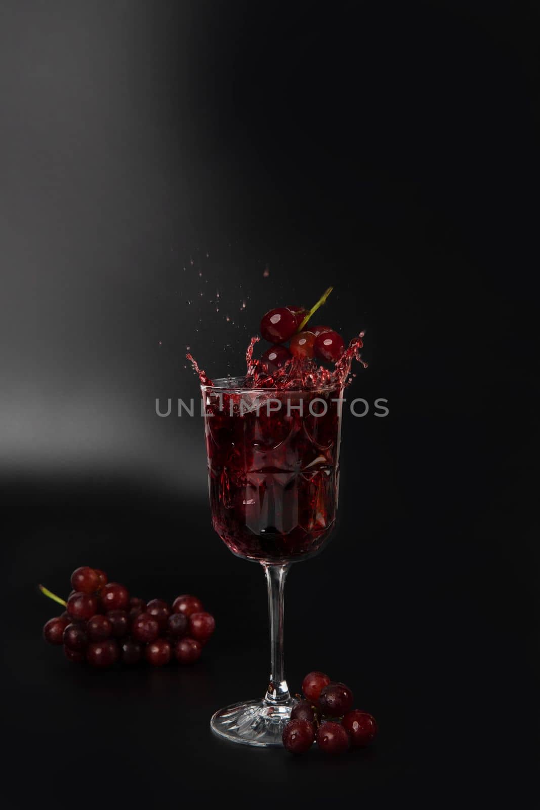 Red wine is poured into a wine glass on a black background with grapes and splash copy space