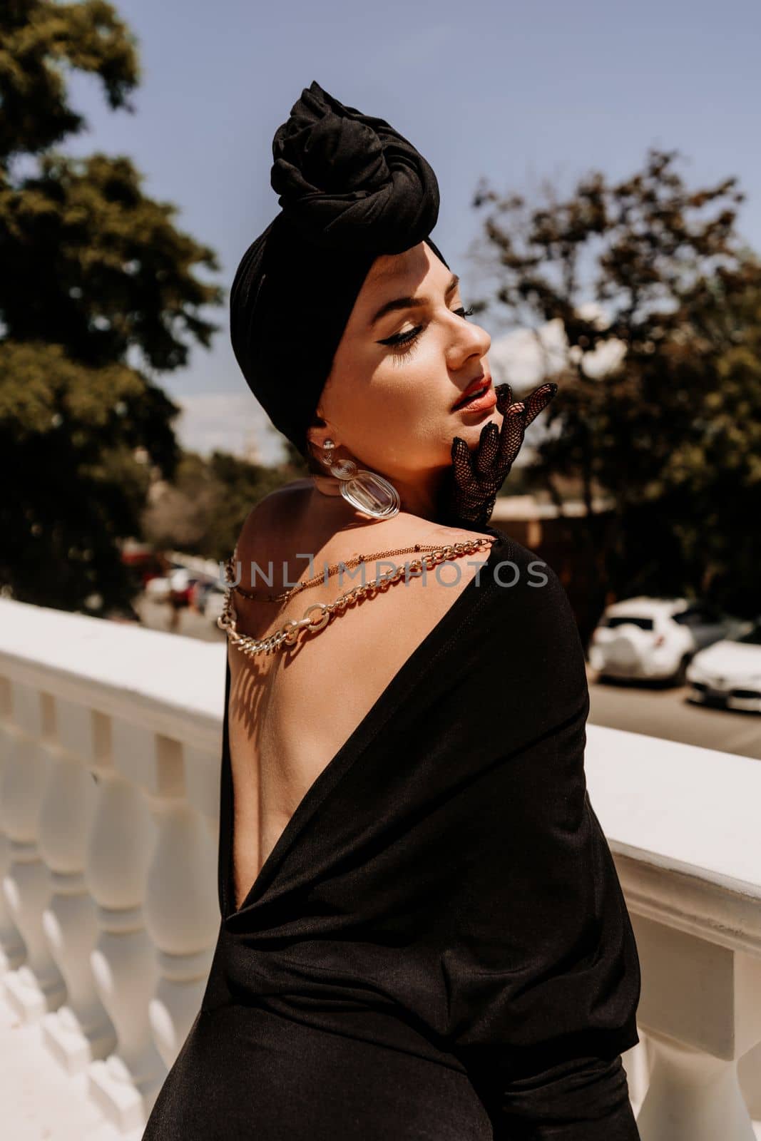 Stylish woman in the city. Fashion photo of a beautiful model in an elegant black dress posing against the backdrop of a building on a city street.