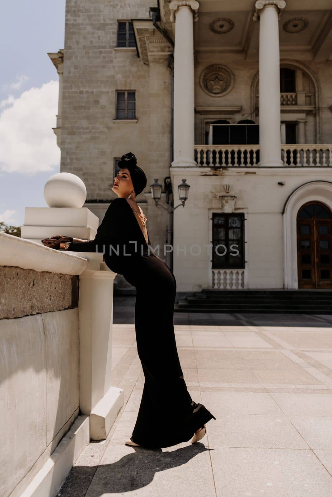 Stylish woman in the city. Fashion photo of a beautiful model in an elegant black dress posing against the backdrop of a building on a city street.