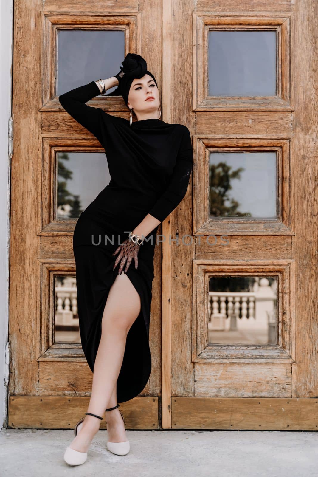 Stylish woman in the city. Fashion photo of a beautiful model in an elegant black dress posing against the backdrop of a building on a city street.