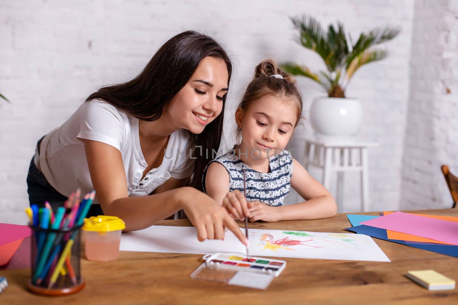 Happy family. Mother and daughter together paint. Woman helps the child girl.