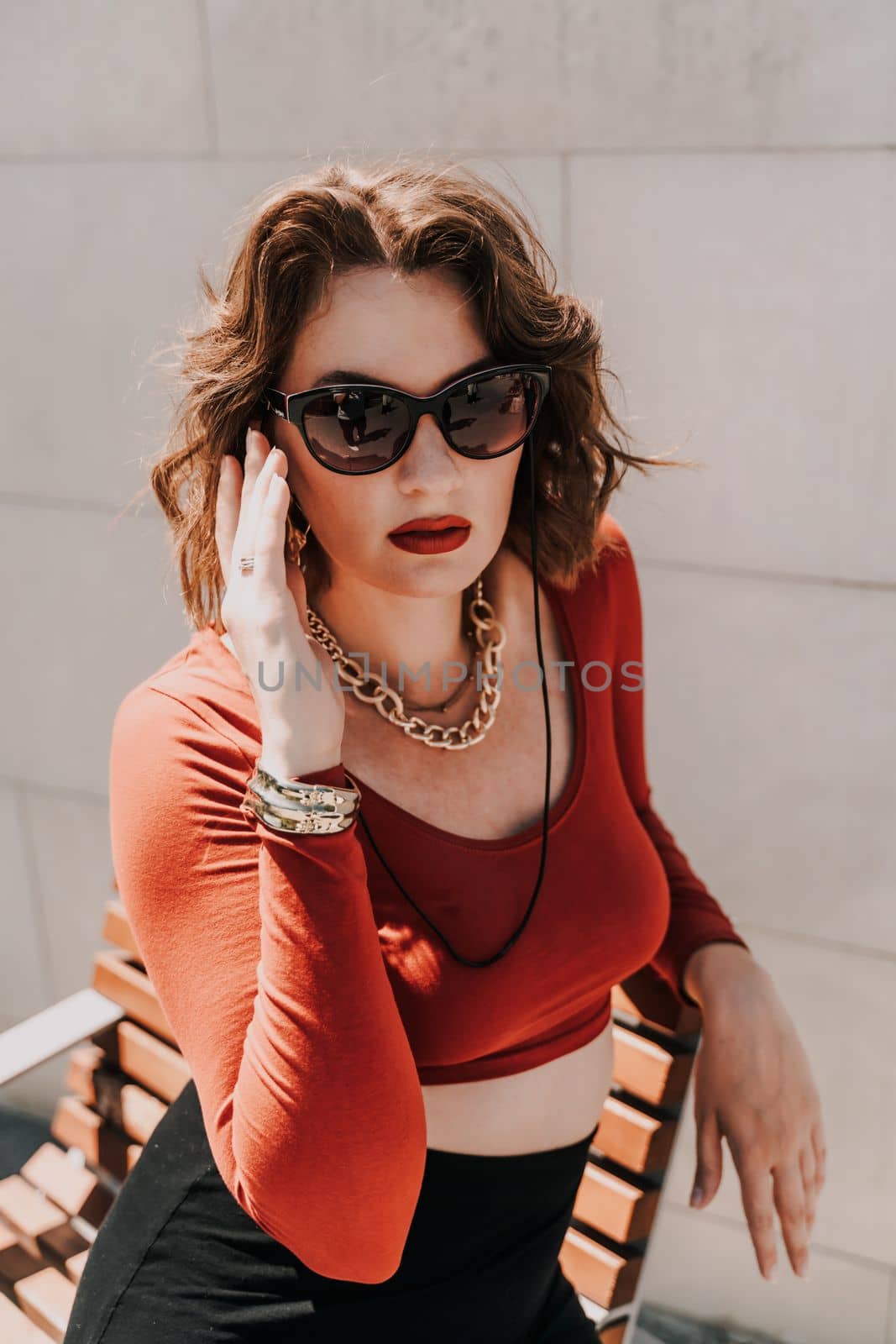 Portrait of a woman on the street. An attractive woman in glasses, a red blouse and a black skirt is sitting on a bench outside