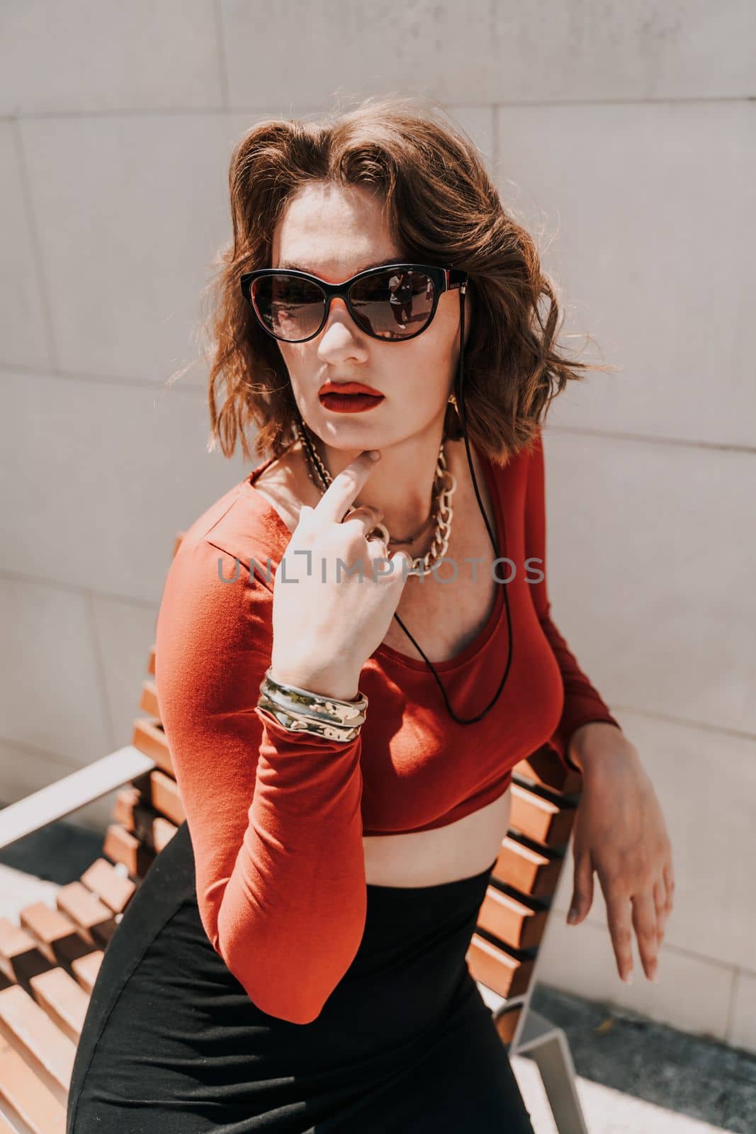 Portrait of a woman on the street. An attractive woman in glasses, a red blouse and a black skirt is sitting on a bench outside