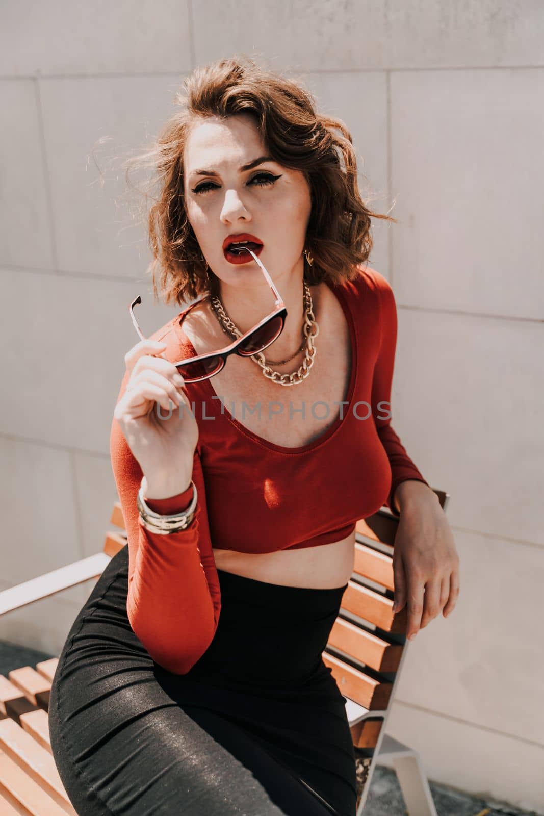 Portrait of a woman on the street. An attractive woman in glasses, a red blouse and a black skirt is sitting on a bench outside