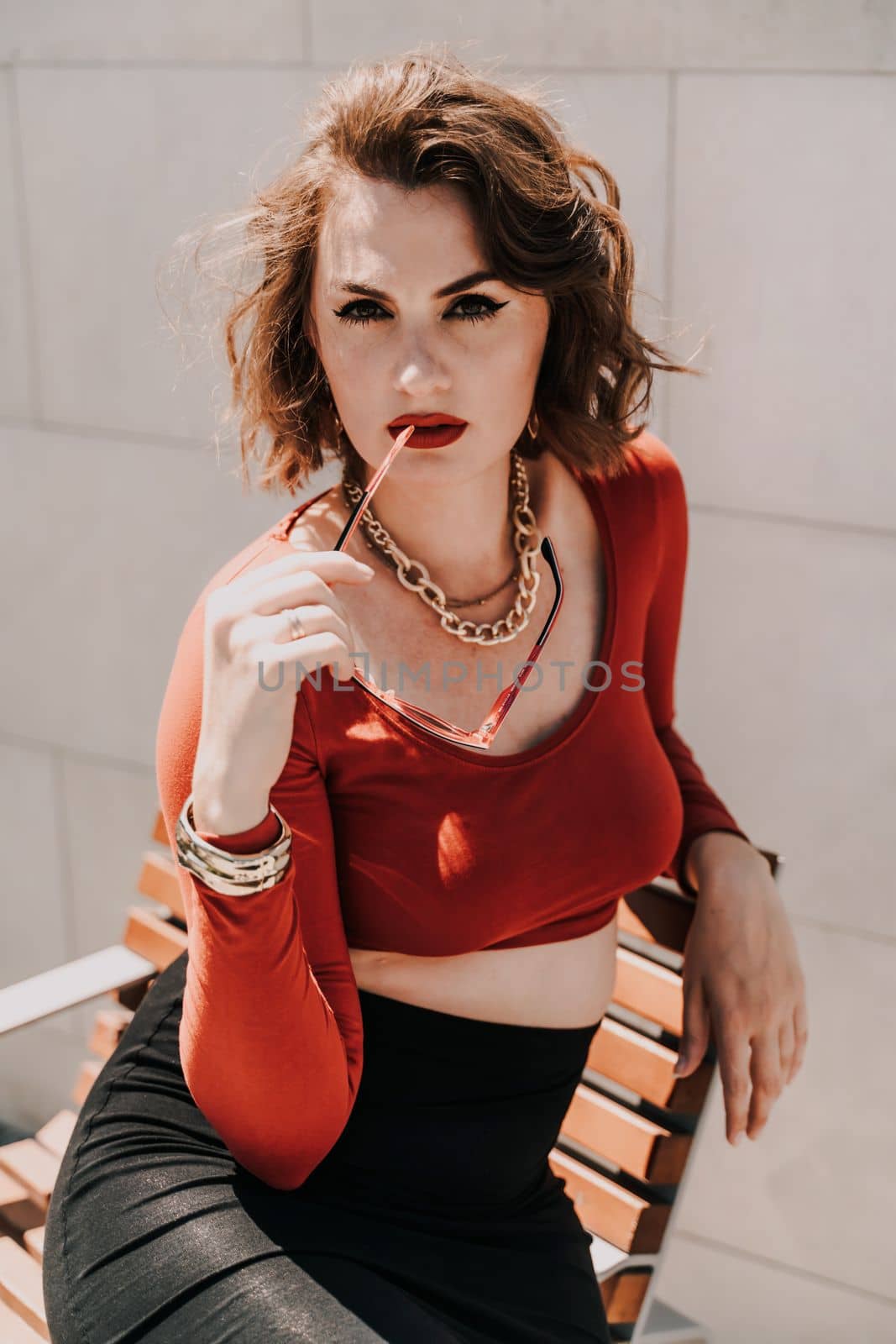 Portrait of a woman on the street. An attractive woman in glasses, a red blouse and a black skirt is sitting on a bench outside