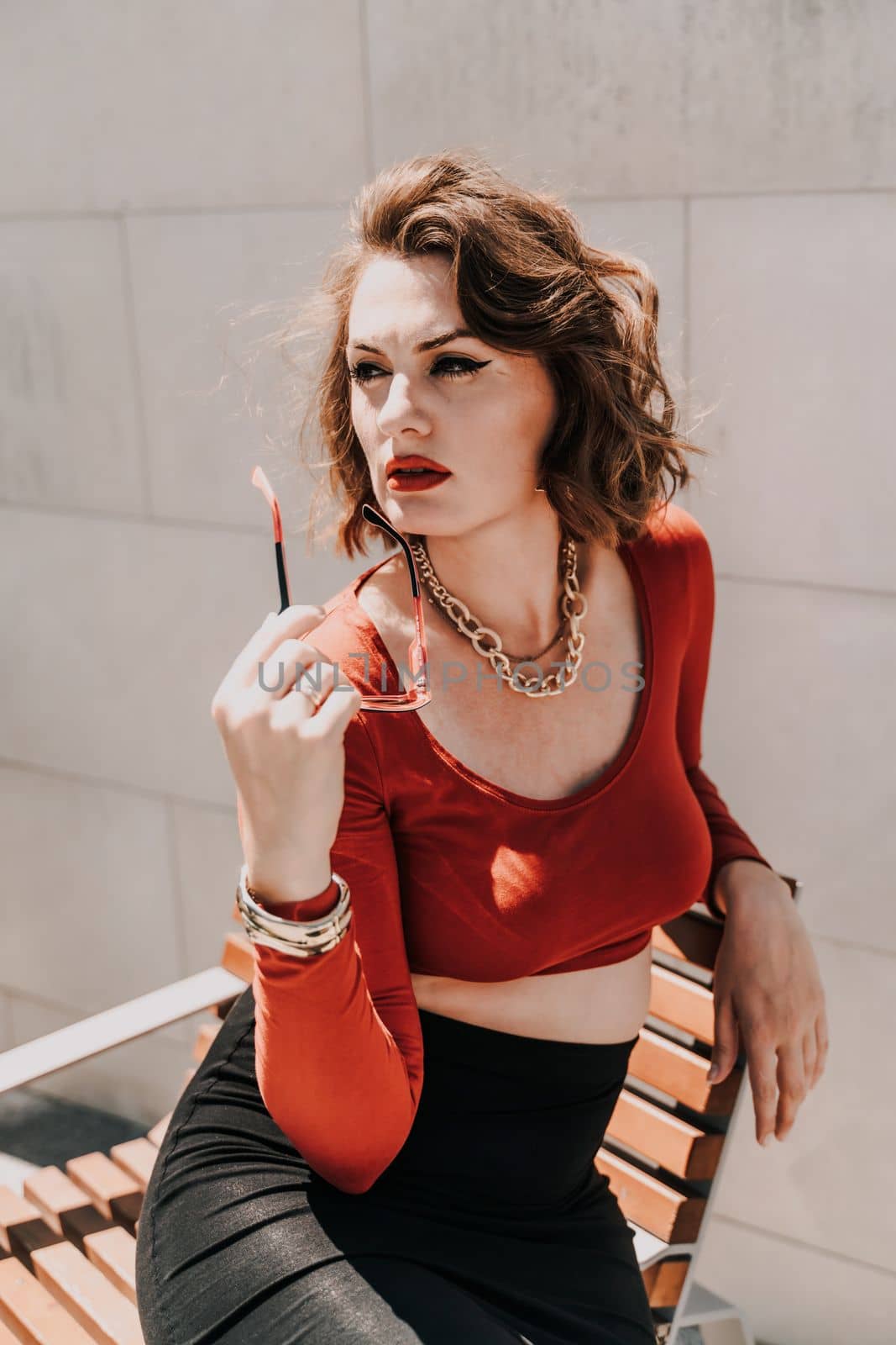 Portrait of a woman on the street. An attractive woman in glasses, a red blouse and a black skirt is sitting on a bench outside